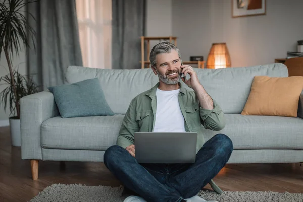 Smiling Caucasian Retired Male Beard Sits Floor Laptop Calls Phone — Foto de Stock