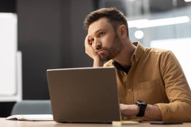 Professional Burnout. Unhappy Business Man Sitting Bored Near Laptop In Modern Office. Apathic Male Worker Having Depression And Business Problems At Workplace