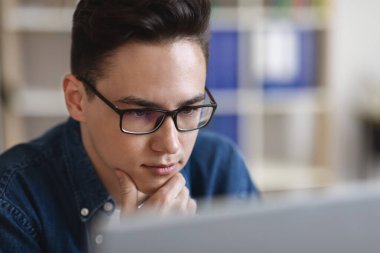 Gözlüklü, bilgisayar ekranına bakan yakışıklı bir adamın portresi, ofiste dizüstü bilgisayarla çalışan, e-posta ya da iş mektubu okuyan, seçici odaklı,