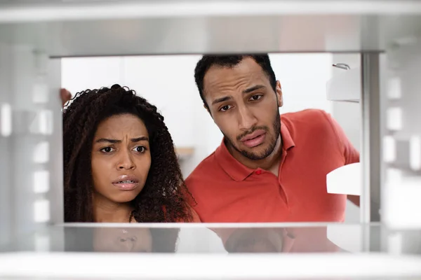 Hungry unhappy upset young african american woman and man check empty fridge in kitchen. Whats for dinner. Facial expression, crisis, sad emotions, diet and no food at home, close up