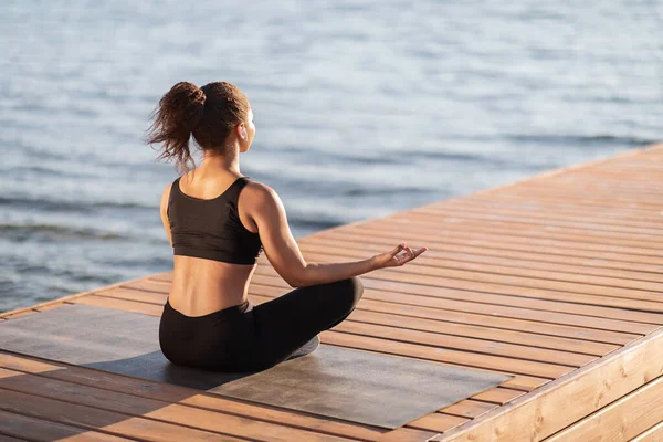 Yoga, stres atma, açık hava aktivitesi. Tanımlanamayan Afro-Amerikan kadın siyah spor giyimli Lotus pozisyonunda fitness minderinde oturuyor, kamu parkında meditasyon yapıyor, yer kopyalıyor.