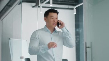 Business conflicts concept. Emotional middle aged asian businessman talking with partners via cellphone, discussing problem solution distantly from office, slow motion