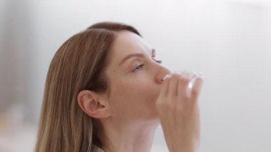 Runny nose treatment. Close up portrait of sick middle aged woman using nasal drops at home, smiling after relief effect, slow motion