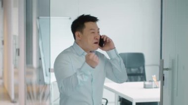 Olumlu telefon konuşması. İş arkadaşlarıyla konuşan, harika haberlerin tadını çıkaran, gülen, ofiste ağır çekimde duran orta yaşlı Asyalı adamın kapalı bir portresi.