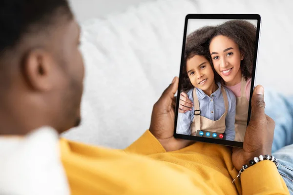 Virtual Meeting. Unrecognizable black man having video call with wife and daughter, african american male using digital tablet while relaxing on couch, communicating online with family, collage