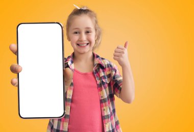Cute Happy Little Girl Holding Big Blank Smartphone And Showing Thumb Up, Cheerful Excited Female Child Recommending New Mobile App Or Website, Standing On Yellow Background, Collage, Mockup
