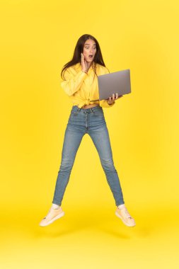 Şok Olan Kadın Dizüstü bilgisayarın Sarı Stüdyo Arkaplanından Atlarken Dikey Çekimi. Bilgisayar okuyan kadın pozu şok edici haberler. Harika Web Sitesi Reklamı