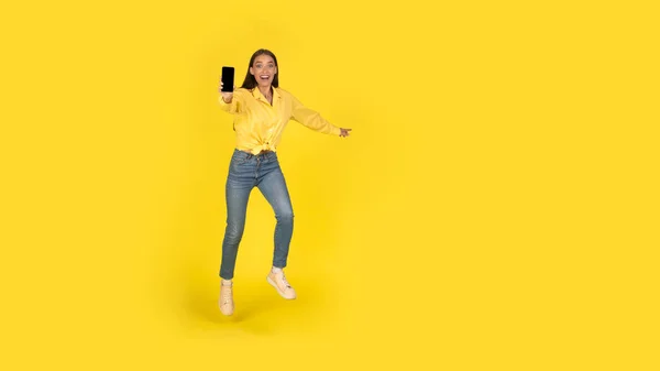 Excited Woman Showing Phone Jumping Posing Yellow Studio Background Female — Stock Fotó