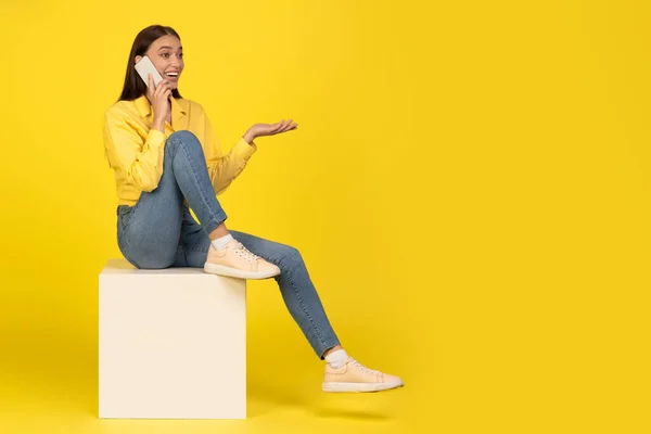 Cheerful Woman Talking Phone Sitting Cube Yellow Background Studio Shot — Stock Fotó