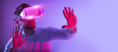 Yüksek teknoloji eğlence konsepti, kolaj. Sanal gerçeklik gözlüklü sakallı genç adam neon arka planda görünmez bir şeye dokunuyor, kopya alanı olan bir panorama, web-pankart