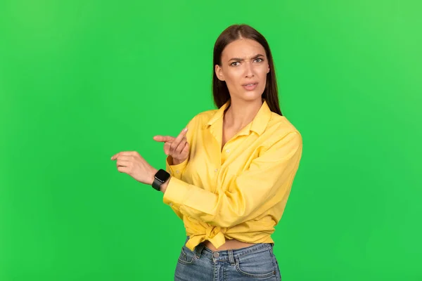 Deadline. Displeased Female Pointing Finger At Smartwatch On Hand Posing Over Green Studio Background, Looking At Camera. Punctuality Problems, Time Management Concept