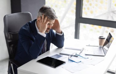 Troubles At Work. Stressed Mature Businessman Sitting At Desk In Office And Touching Head, Depressed Middle Aged Man In Suit Suffering Financial Problems Or Business Failure, Free Space