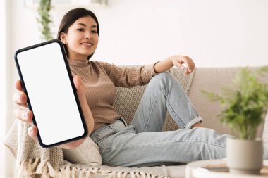 Mobil Teklif. Gülümseyen Asyalı Kadın, evde koltukta otururken kamerada büyük boş akıllı telefonu gösteriyor, Millennial kadın elinde büyük bir cep telefonu, beyaz ekran, kolaj, model