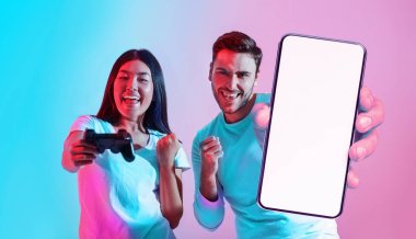 Güzel uygulama. Heyecanlı çoklu etnik çeşitliliğe sahip çift boş akıllı telefon, joystick reklam uygulaması ya da web sitesi olan neşeli kadın ve erkek stüdyoda neon ışığı altında beklerken, kolaj, model