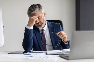 Overworking Concept. Tired Mature Businessman Suffering Headache During Work In Office, Exhausted Middle Aged Entrepreneur Taking Off Glasses And Massaging Nose Bridge, Feeling Unwell At Workplace