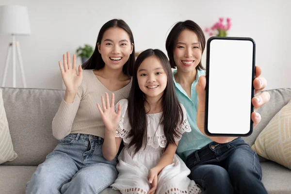 Mutlu Asyalı büyükanne, anne-kız el sallıyor ve evdeki kanepede otururken boş akıllı telefon gösteriyor. Çok nesildir aile yeni mobil uygulama, kolaj, modelleme öneriyor.