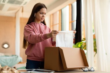 Hüsrana uğramış genç kız, karton kutuları yatak odasının içinde açıyor, boş yer var. Çevrimiçi alışveriş siparişinde hata, mal teslimatında sorun