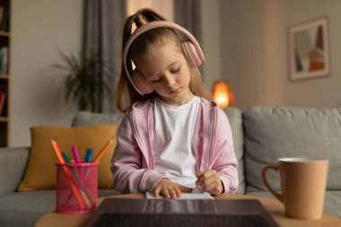 Yorgun Öğrenci Kız İnternette dizüstü bilgisayar kullanarak evde masa başında otururken not alıyor. Kablosuz kulaklık takan, yazı yazan bilgisayar ödevi yapan bir kız. E-Öğrenme, Modern Eğitim Konsepti