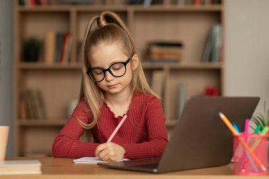 E-öğrenme. Gözlük takan, dizüstü bilgisayar kullanan ve evde otururken not alan liseli kız. Modern Uzaktan Eğitim ve Eğitimsel İnternet Hizmetleri Kavramı