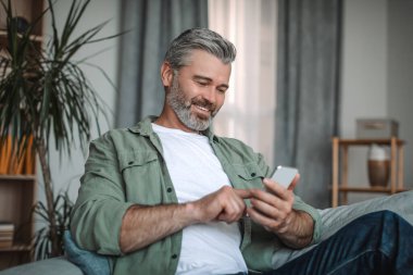 Sakallı, akıllı telefonuyla yazı yazan neşeli, yaşlı Avrupalı bir adam. Oda içinde sosyal medya sohbetinin keyfini çıkarıyor. Sosyal uzaklık ve yeni uygulama, evde bulunan emekliler için covid-19 salgını için aygıt