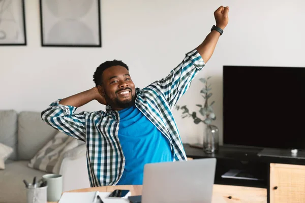 Successful Freelance Career. Relaxed Black Man Stretching Hands After Successful Work Day Sitting At Laptop Computer At Home. Remote Job, Internet Business And Technology Concept