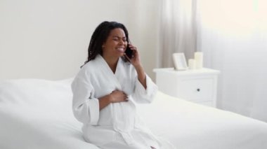 Acil durum çağrısı. Genç mutsuz hamile Afro-Amerikan kadın akut karın ağrısı çekiyor, acil yardım için doktoru arıyor, evde yatıyor, ağır çekimde, boş alanda.