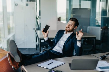 Aşırı mutlu iş adamı ofiste dinleniyor, ayaklarını masaya koyuyor ve kulaklıkla müziğin keyfini çıkarıyor, cep telefonunu tutuyor ve dans ediyor, işe ara veriyor, boşluğu kopyalıyor.