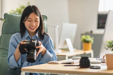 Cheerful Japanese Lady Photographer Holding Photocamera At Workplace. Woman Learning To Take Photos Posing With Camera Sitting In Chair Indoor. Creative Photography, Career And Education Concept