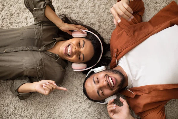 Cheerful Black Couple Wearing Headphones Listening Music Online Lying Floor — ストック写真