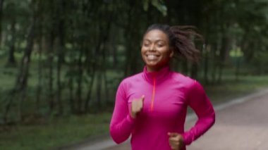 Preparing to marathon. Outdoor portrait of happy active african american woman athlete running in public park, enjoying sport training, follow shot, slow motion, empty space