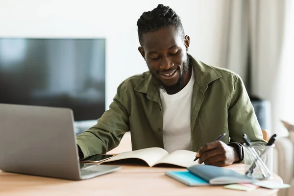 Smiling African American Man Sitting Desk Working Laptop Taking Notes —  Fotos de Stock