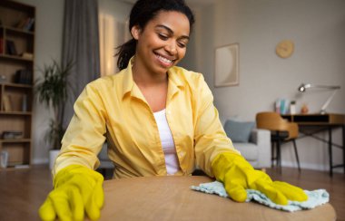 Neşeli Afro-Amerikan Kadın Toz Masası Masası Temizleme Masası, evde ahşap mobilya bakımı yapan, sarı lastik eldivenler giyen. Ev işleri ve ev işleri. Seçici Odaklanma
