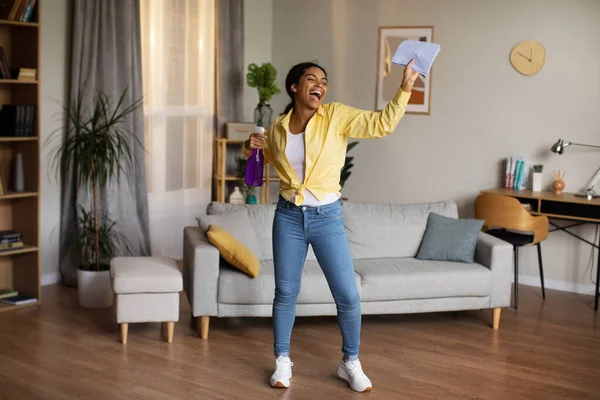 Happy Black Female Singing Holding Rag And Detergent Spray Bottle Cleaning Living Room And Having Fun Standing At Home. House Chores Leisure. Full Length Shot