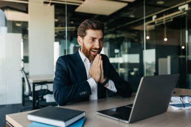 Excited businessman celebrating great news and luck, looking at laptop screen in joy, sitting at workplace in modern office interior. Got job promotion, win concept