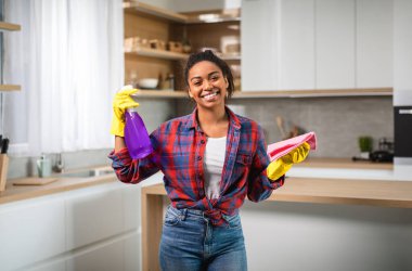 Bin yıllık lastik eldivenli siyah bir kadının sprey sıkması, paçavra giymesi, temizlik yapması, profesyonel temizlik malzemelerini mutfak içini temizlemek için kullanması güzel. Ev işleri, ev işleri.
