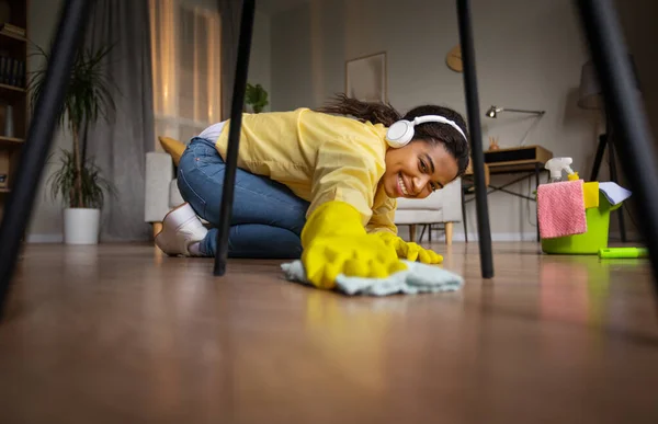 Happy Black Lady Dusting And Mopping Floor With Rag Under Table Cleaning Modern Living Room At Home, Wearing Rubber Gloves. Female Doing House Chores. Selective Focus