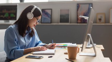 Asyalı iş kadınının bilgisayar ekranının önünde oturmuş kulaklık takıp iş yaparken ya da içeride öğrenirken görüntüsü. İş Kariyeri Konsepti. Panorama