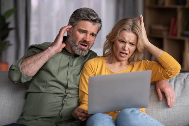 Şok İçeriği. Hüsrana uğramış Orta Çağ Eşleri dizüstü bilgisayara bakıyor, Duygusal Erkek ve Kadın Kötü Haberler 'i okuyor, Kafası karışmış çift evde bilgisayar başında oturuyor,