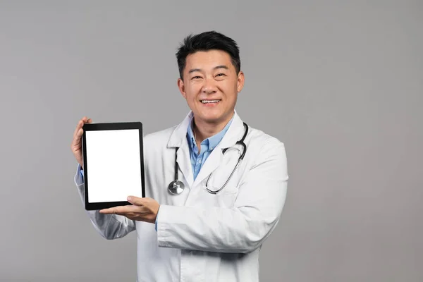 Smiling Mature Chinese Doctor White Coat Stethoscope Showing Tablet Blank — Zdjęcie stockowe