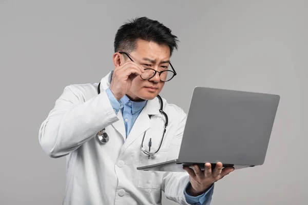 Zmatený Dospělý Asijský Lékař Bílém Plášti Sundá Brýle Podívá Notebook — Stock fotografie