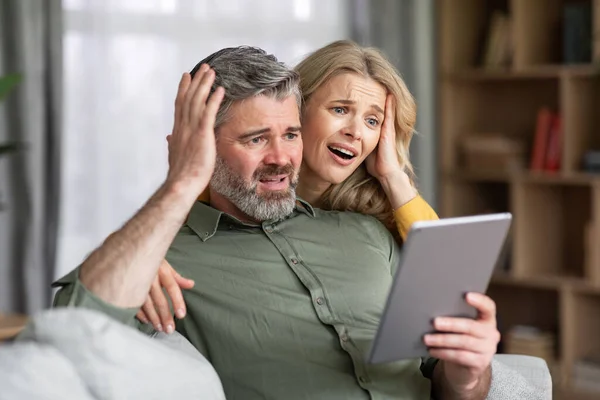 Shocked Middle Aged Spouses Looking Digital Tablet Screen Home Confused — Zdjęcie stockowe