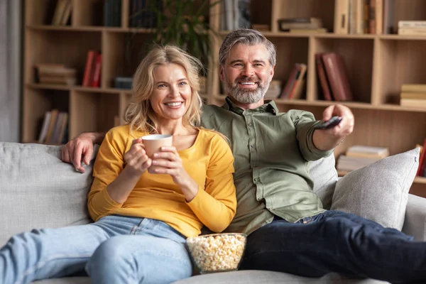 Home Relax. Happy Married Middle Aged Couple Watching Tv In Living Room, Smiling Spouses Eating Popcorn And Drinking Coffee Together While Relaxing On Comfortable Couch, Closeup Shot