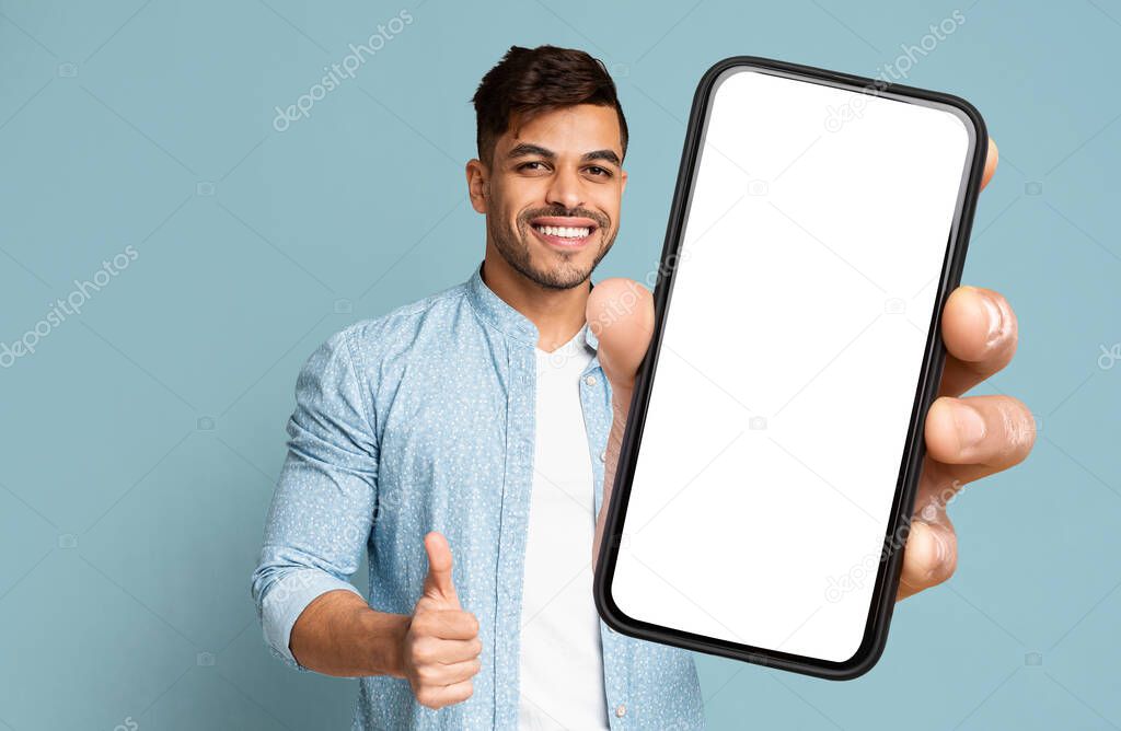 Handsome Middle Eastern Young Man Showing Modern Cell Phone With White Empty Screen And Thumb Up On Blue Studio Background. Free Space And Mockup For Advertisement, Collage