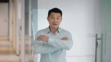 Corporate career concept. Successful middle aged asian businessman posing at office building, crossing hands and smiling to camera, slow motion, free space