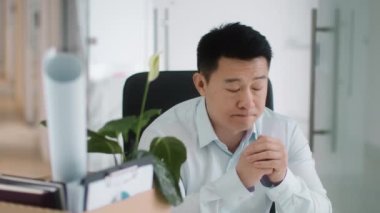 Last day at work. Close up portrait of depressed dismissed asian middle aged man sitting at office, looking at personal belongings at box and deeply breathing, slow motion