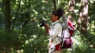 Aktif yaratıcı hobi. Ormanda yürüyen ve doğayı yakalayan, sırt çantasıyla yürüyüş yapan, çekimleri takip eden, yan görüş, yavaş çekim yapan Afrikalı Amerikalı genç bir turist.