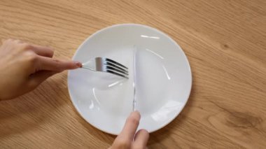 Açlık krizi konsepti. Kadın ellerinin bıçak ve çatalla görünmeyen yiyecekleri boş tabakta keserken, yavaş çekim görüntüsü.
