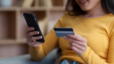 Dijital finans konsepti. Asyalı genç bir kadının internet üzerinden para transferi ya da ödeme yaparken, akıllı telefon ve kredi kartı, yavaş çekim ve boş alan kullanarak yakın plan çekimleri.