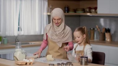 Evde aşçılık dersi. Mutlu Müslüman anne tesettürlü küçük kızıyla fırın yapıyor, mutfakta hamuru birlikte yoğuruyor, yavaş çekim, serbest alan