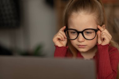 Zavallı görme duyusu. Gözlüklü, dizüstü bilgisayara bakan ve evde oturup ödevlerini yapan bir çocuk. Çocuk Gözü Sağlığı Konsepti. Seçici Odaklanma